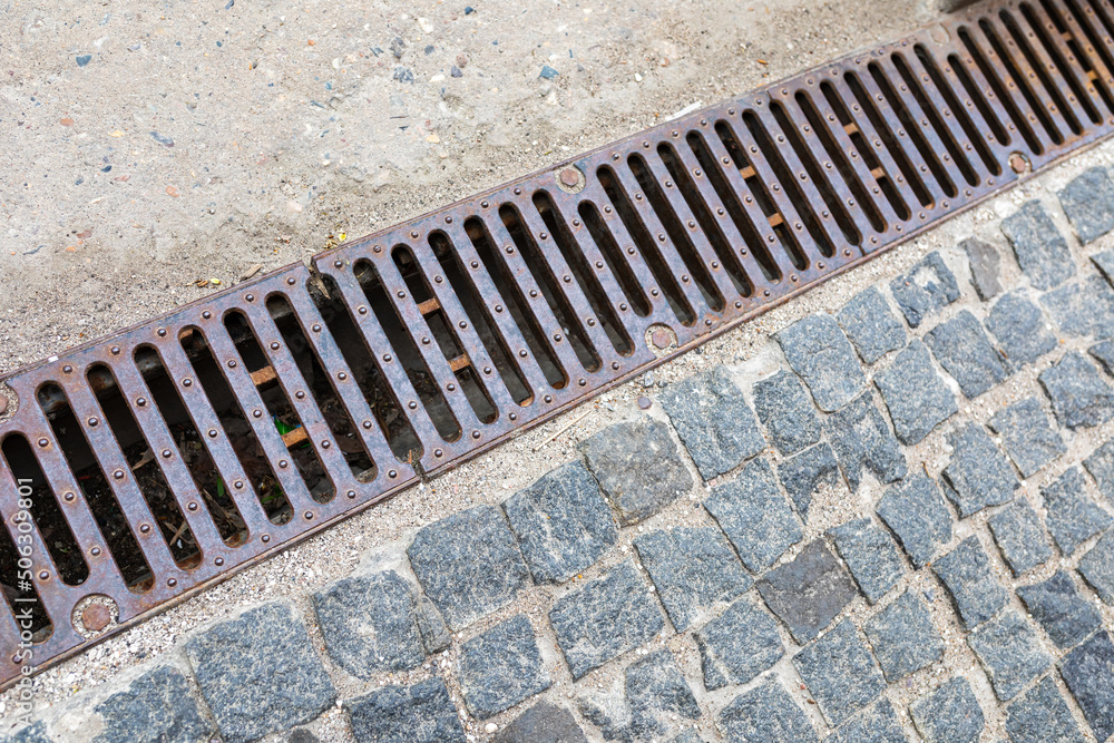 Grating of drainage system rainwater in the park at the sidewalk from a stone shaped paving slabs