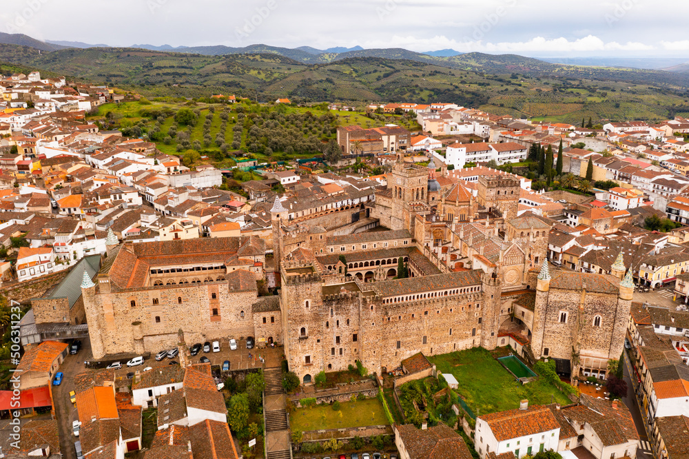 Picturesque aerial view of majestic architecture of ancient Roman Catholic Monastery of Saint Mary of Guadalupe surrounded by residential buildings with brownish tiled roofs on spring day, Spain