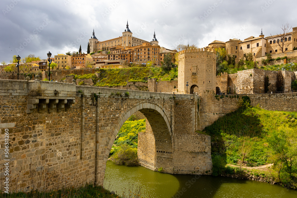 Picturesque landscape with a view of the Alcantara Bridge, spanning the Tagus River, and the ancient Alcazar de Toledo ..Castle, located in the upper part of the city of Toledo, Spain - obrazy, fototapety, plakaty 