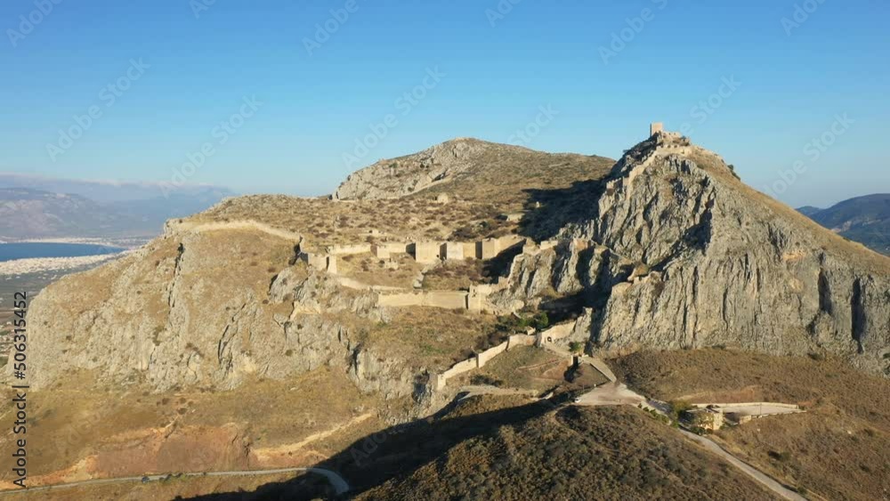 A road leads to the ancient and majestic Acrocorinth in Europe, Greece, the Peloponnese, towards Corinth, in summer, on a sunny day. A road leads to the ancient and majestic Acrocorinth in Europe, Greece, the Peloponnese, towards Corinth, in summer, on a sunny day.