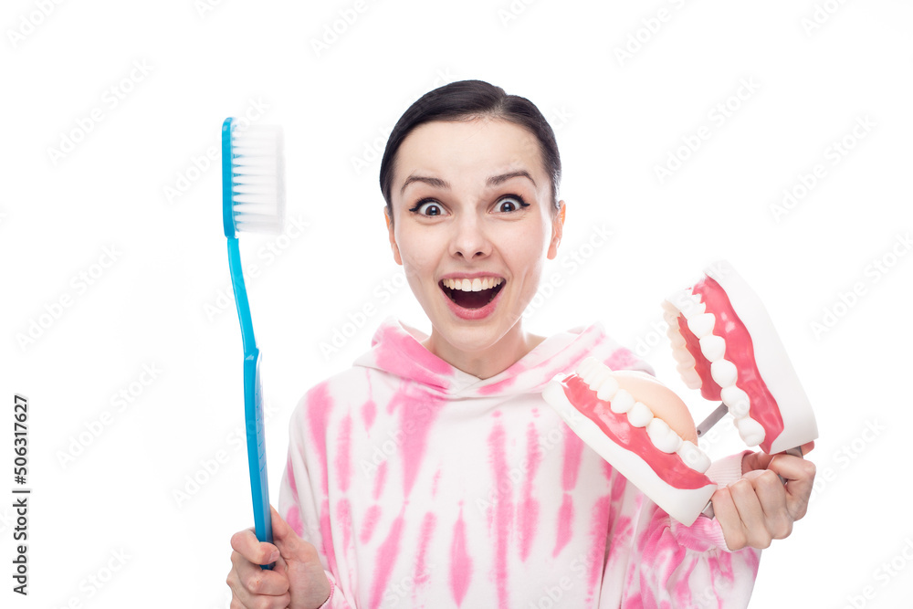 joyful woman in a pink sweatshirt with a huge blue toothbrush and a tooth jaw in her hands joyful woman in a pink sweatshirt with a huge blue toothbrush and a tooth jaw in her hands