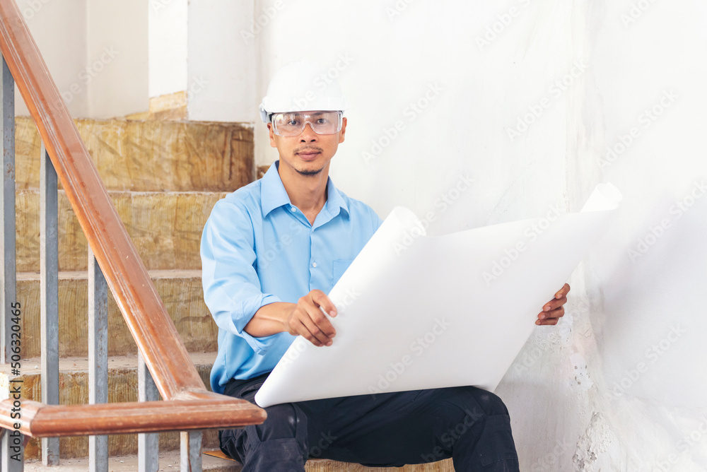 Construction engineer man hold blueprint wear blue shirt safety white hard hat at construction site industry labor worker. Architecture man engineer civil worker look at blueprint real estate concept Construction engineer man hold blueprint wear blue shirt safety white hard hat at construction site industry labor worker. Architecture man engineer civil worker look at blueprint real estate concept
