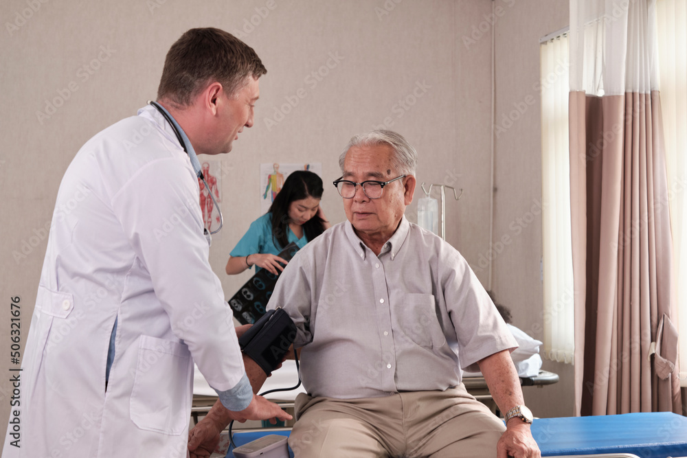 Obraz premium Caucasian male doctor in uniform health checks illness senior patient, blood pressure by measure gauge in emergency room bed at hospital ward, elderly medical clinic, painful examination consultant.