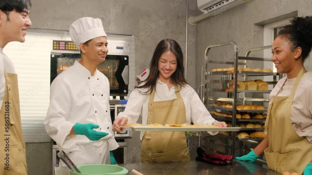 Young Asian female cooking class student shows tray of baked pies from oven, good smell for group of chefs, happy pastry cuisine in culinary course lesson, food occupation in stainless steel kitchen. Young Asian female cooking class student shows tray of baked pies from oven, good smell for group of chefs, happy pastry cuisine in culinary course lesson, food occupation in stainless steel kitchen.