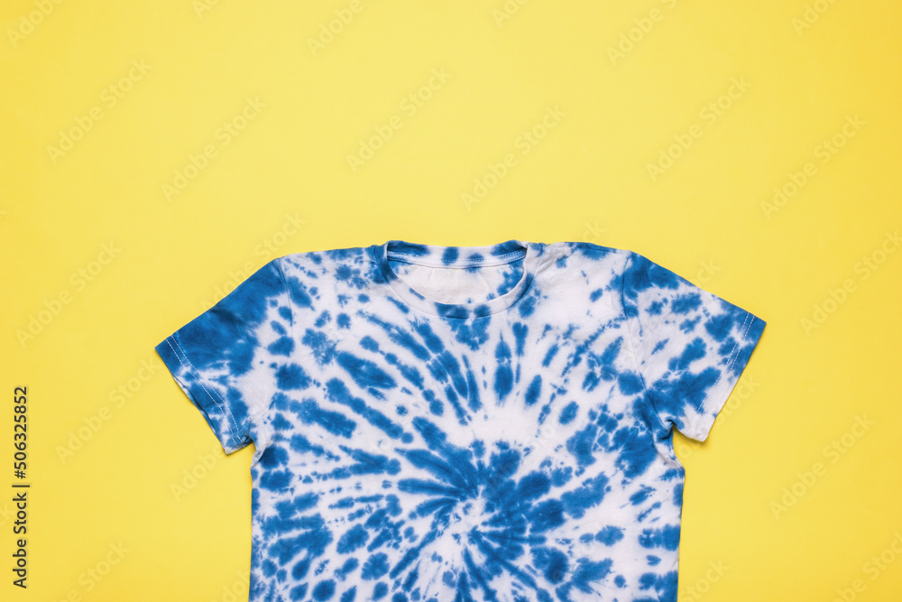 Blue tie dye T-shirt on a yellow background. Flat lay. - obrazy, fototapety, plakaty 