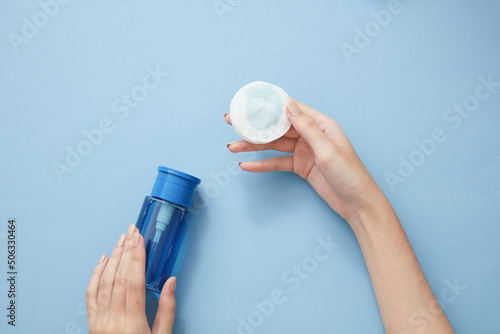 Slika na platnu Topview of hand model using makeup remover on cotton pad in blue background for