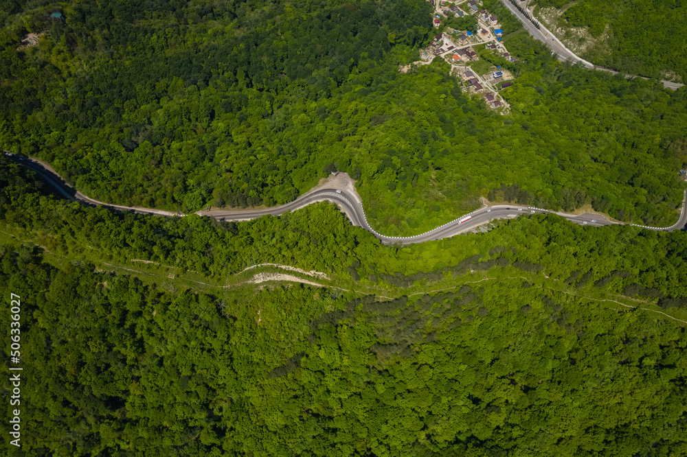 Aerial view of winding road from the high mountain pass. Great road trip trough the dense woods. Birds eye view.