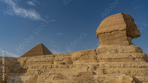 Sculpture of the Great Sphinx against the blue sky. Close-up. Profile view. The layered structure of the statue, the masonry is visible. The top of the pyramid above the back. Egypt. Giza
