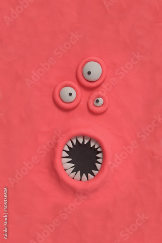 Monster with three ugly eyes and a mouth with sharp teeth, fabulous creature made by hand from pink plasticine. Comic facial expressions. Ugly and crazy face of alien monster. 3d artwork