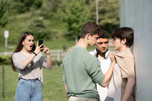 Two bullies menacing teenager boy and girl filming on phone. Cyber bullying and violence concept.