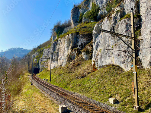 Fotografie Electric railway track running on rocky mountainside, penetrating tunnel, sunny