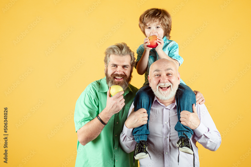 Grandfather father and son hugging and eating apple. Men in different ages, isolated on yellow.