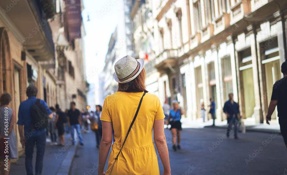 Woman walking on street. Woman tourist in yellow dress with hat walking on street of Rome on sunny day.
