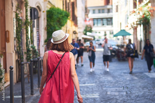 Woman walking on street. Woman tourist in red dress with hat walking on street of Rome on sunny day.
