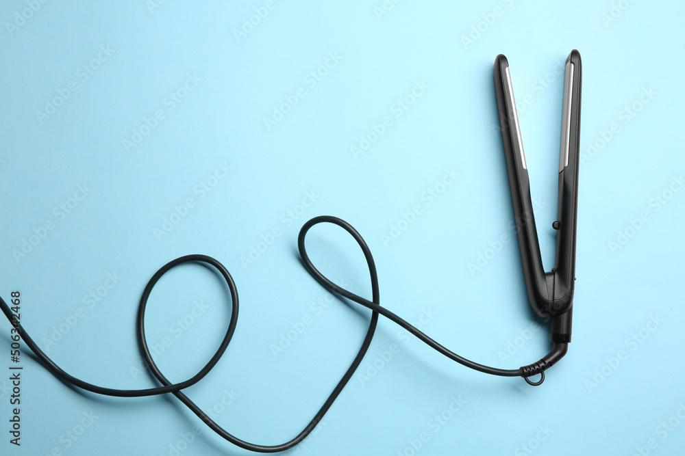 Modern flat hair iron on light blue background, top view Modern flat hair iron on light blue background, top view