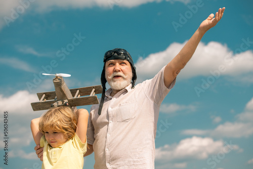 Grandfather and grandson with plane over blue sky and clouds background. Men generation grandfather and grandson playing outdoors.