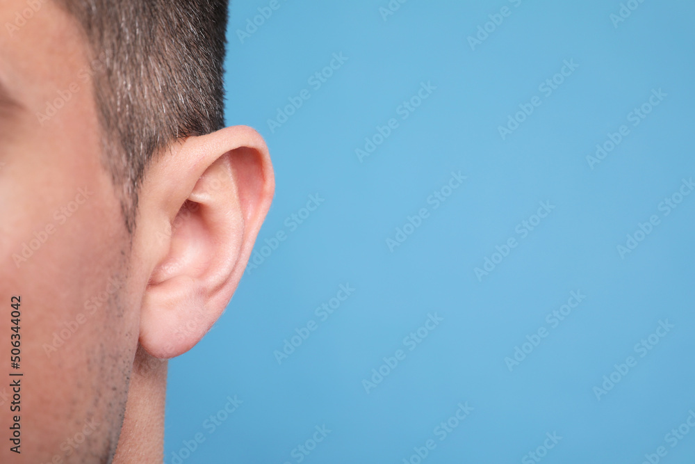 Fototapeta premium Man on light blue background, closeup of ear. Space for text