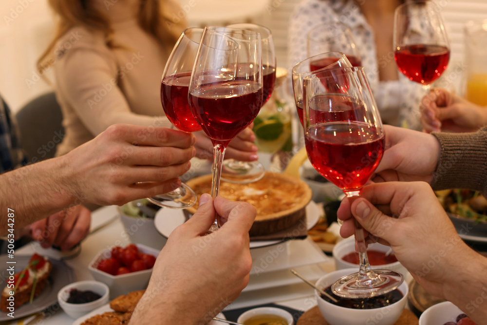 Group of people clinking glasses with red wine during brunch at table indoors, closeup