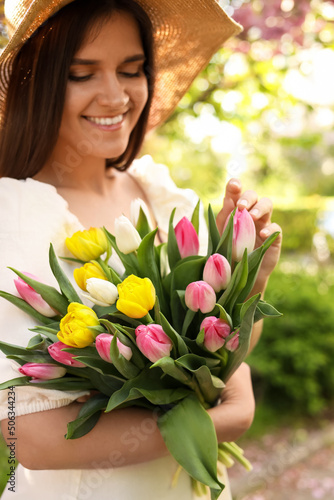 Beautiful young woman with bouquet of tulips in park, focus on flowers