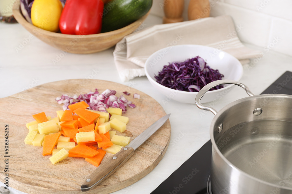 Board with cut vegetables and knife on white countertop in kitchen Board with cut vegetables and knife on white countertop in kitchen