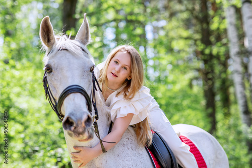 Teenage girl with her favorite white horse for a walk in the spring forest. Communication with animals in nature. 