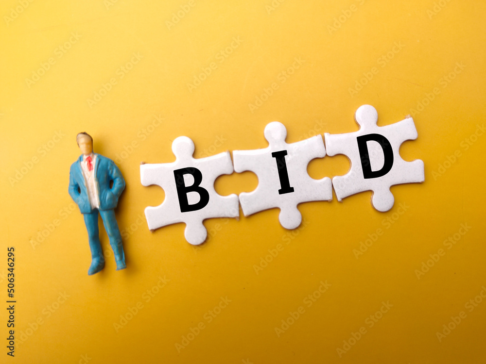 Miniature people and white puzzle with the word BID on yellow background.