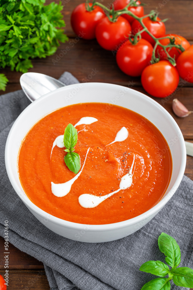 Tomato soup puree in a bowl with cream and fresh basil leaves on a dark wooden background. Copy space. Top view. Tomato soup puree in a bowl with cream and fresh basil leaves on a dark wooden background. Copy space. Top view.