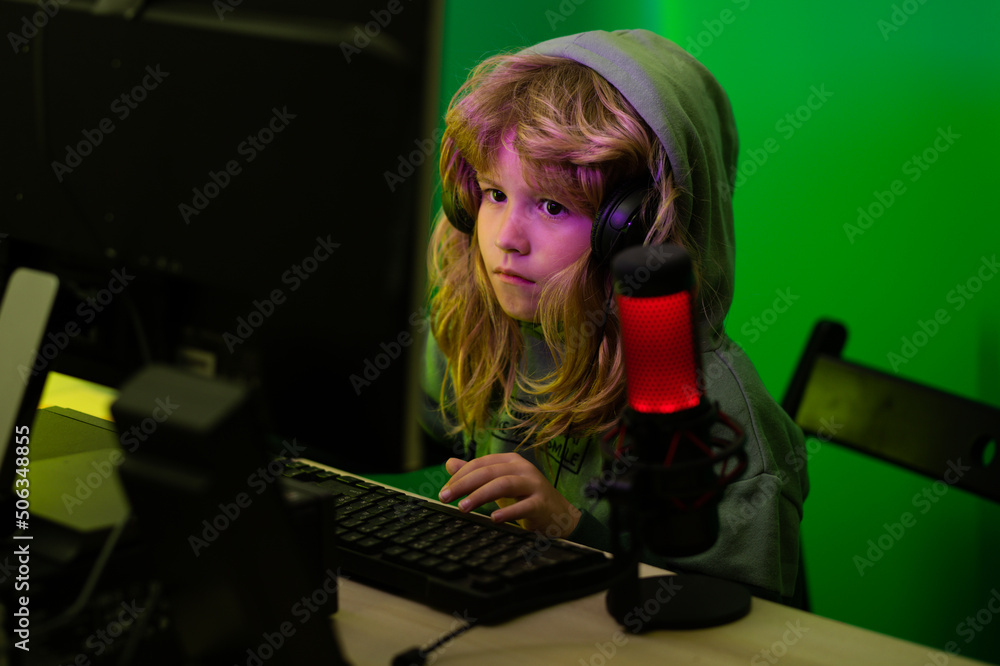 Fototapeta premium Little child gamer play computer game on desktop. Gaming stream and blogging for kids. Child learning online at night, using desktop computer in living room at home.