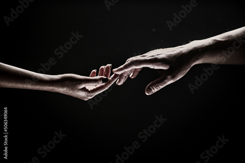 Romantic touch with fingers, love. Two hands stretch each other, black background. Couple in love holding hads, close up. Helping hand, support, friendship. Tenderness, tendet touch. photo