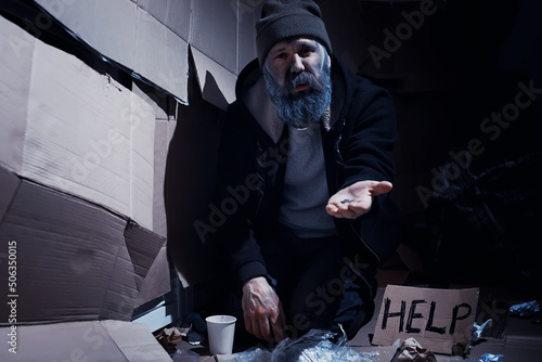 A homeless bearded man sits on boxes on the street and asks for help. Need a homeless person asks for money for food and overnight.