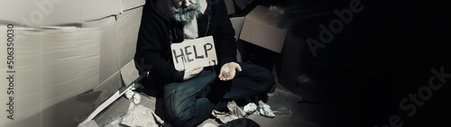Leinwand Poster A homeless bearded man sits on boxes on the street and asks for help