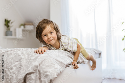 Wallpaper Mural A cute, happy toddler boy lies on the edge of the bed in the bedroom and looks at the camera. Children play at home. Laughter and fun in childhood. Torontodigital.ca