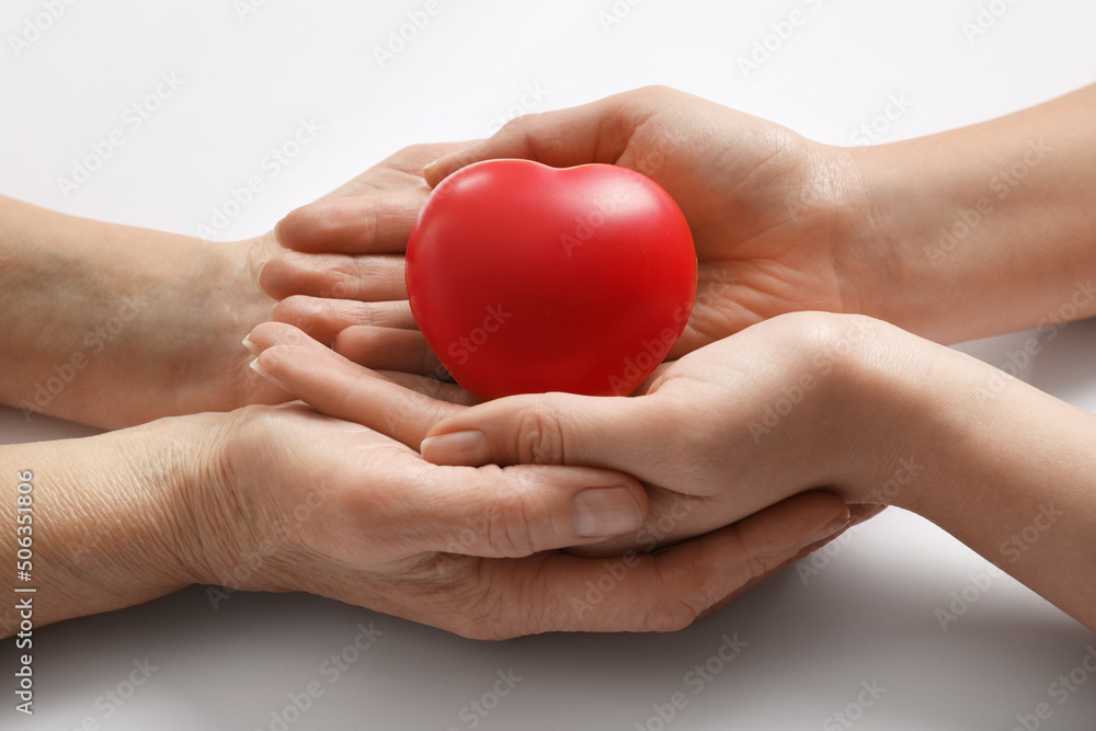 Young and elderly women holding red heart on white background, closeup Young and elderly women holding red heart on white background, closeup