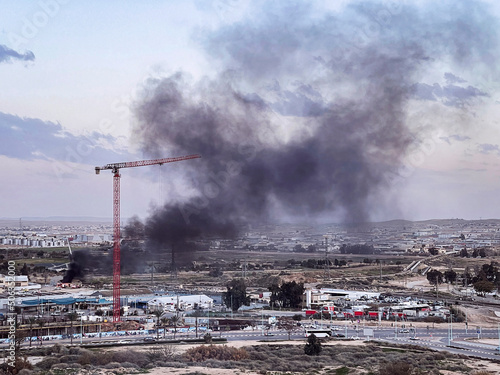 black smoke billows from a small building in an industrial and warehouse district of a city in the Negev region in Israel photo