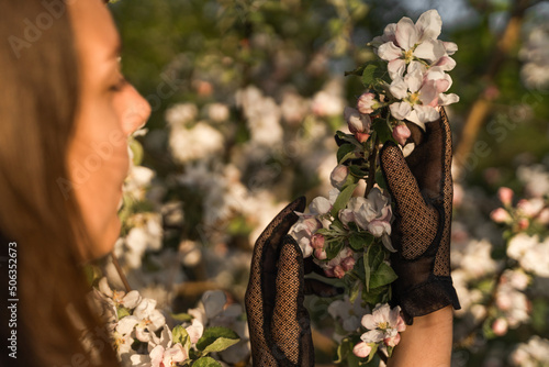 Woman's hands in vintage black lace gloves touching blooming branch of apple tree. Cottagecore concept.