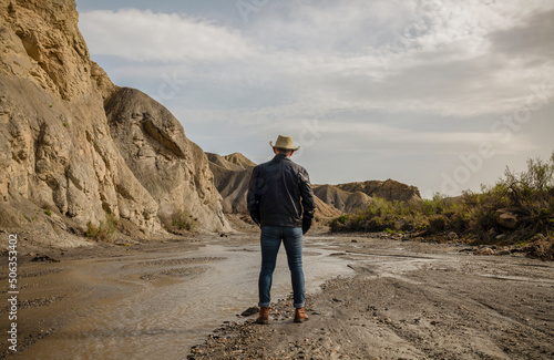 Adult man in cowboy hat in desert against rock and sky