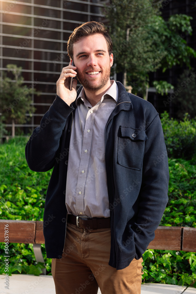 caucasian business man talking on the phone in a park next to an office building, concept of technology and communication caucasian business man talking on the phone in a park next to an office building, concept of technology and communication