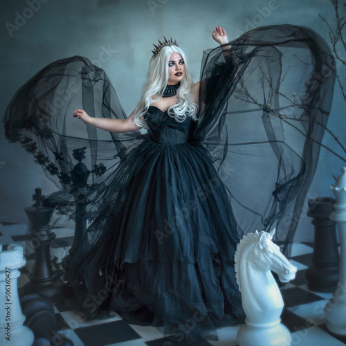 Bilde på lerret A Gothic beauty, a dark evil queen in a black fluffy dress with chess pieces