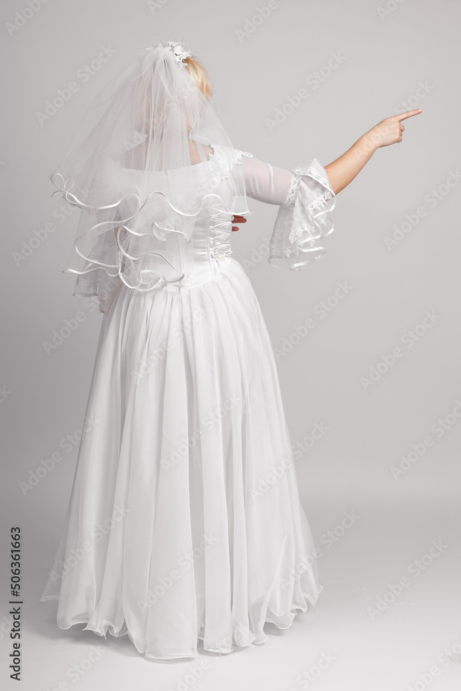 the bride stands with her back in a wedding dress and shows the direction to the side on a white background. full height