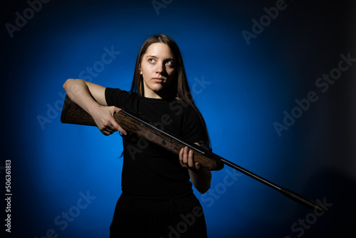 a young girl with long flowing hair in a black T-shirt with a gun in her hands on a dark background
