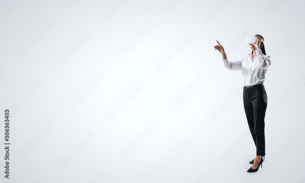 Woman full length standing and working in virtual reality environment in VR glasses, presses by her finger on virtual interface on white backdrop. Innovate and future technology concept, mock up Woman full length standing and working in virtual reality environment in VR glasses, presses by her finger on virtual interface on white backdrop. Innovate and future technology concept, mock up