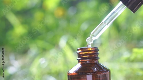 Essential oil falling from glass dropper with medicinal liquid and blur background.