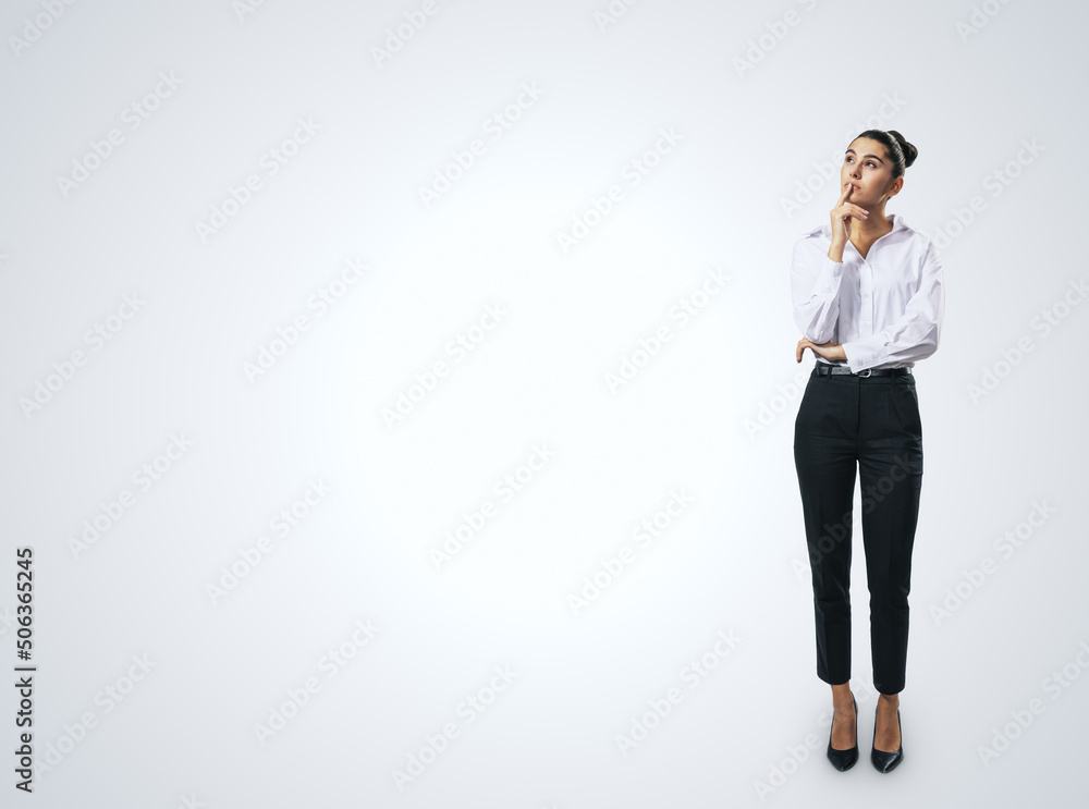 Thinking concept with pensive businesswoman in white shirt and dark trousers standing full length on abstract white wall backdrop, with empty place for you text, mock up Thinking concept with pensive businesswoman in white shirt and dark trousers standing full length on abstract white wall backdrop, with empty place for you text, mock up