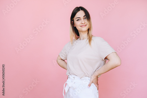 Portrait of a woman posing on a pink background and holding her hands at her sides.