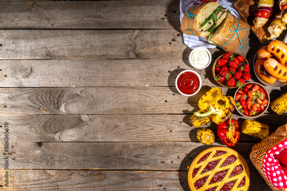 Various picnic barbeque food and drink flatlay. Summer bbq picnic food, assorted grilled meats, kebabs, vegetable, fruit salad, traditional picnic summer pie cake, sandwiches, top view copy space Various picnic barbeque food and drink flatlay. Summer bbq picnic food, assorted grilled meats, kebabs, vegetable, fruit salad, traditional picnic summer pie cake, sandwiches, top view copy space