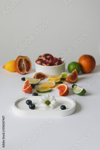 Layout with a white tray with blueberries, flowers and fruits. Oranges, limes, lemons, pomegranate. Background for the product. Flatlay.