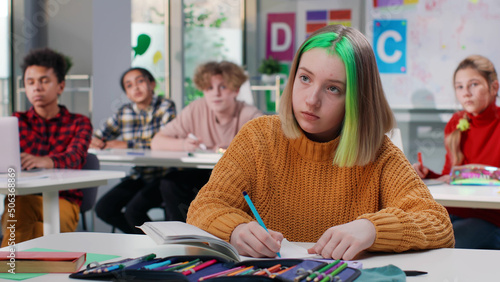 Teenage schoolgirl with green hair writing test in class in school