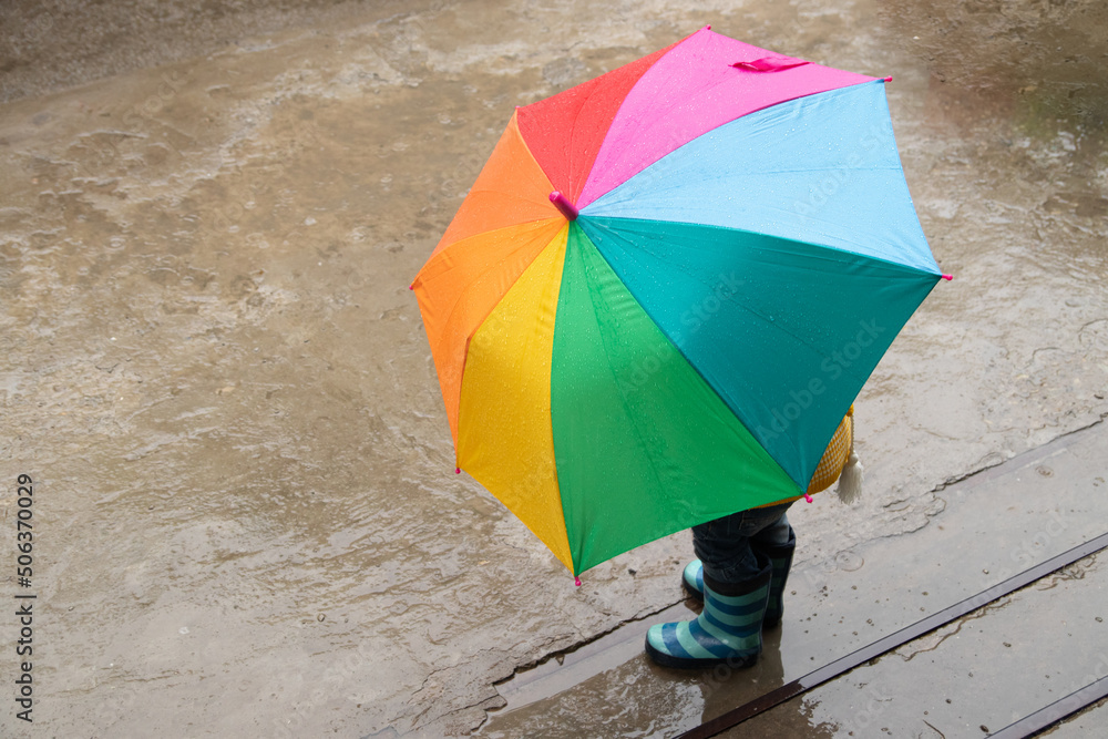 A 3-year-old girl hides in the rain under a colored umbrella