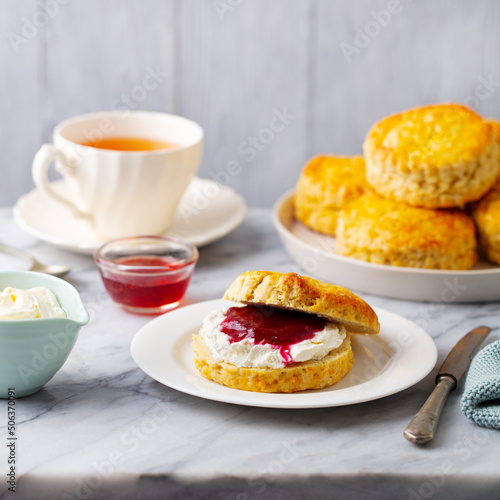 Scones with jam, clotted cream and cup of tea on marble table. Grey background. Close up.