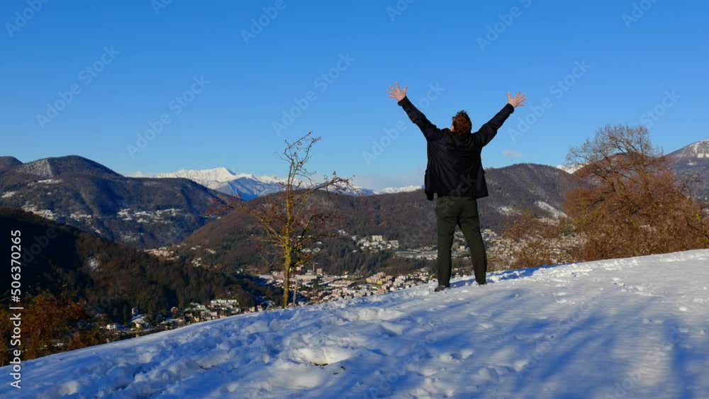 Elegant Man Standing with Arms Raised and Joy Mountain View with Snow and Clear Blue Sky in a Sunny Day in Collina di Oro in Ticino, Switzerland. Elegant Man Standing with Arms Raised and Joy Mountain View with Snow and Clear Blue Sky in a Sunny Day in Collina di Oro in Ticino, Switzerland.